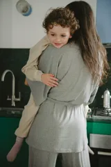 Conjunto de ropa de descanso para maternidad compuesto por un pantalón negro de tiro alto y corte ancho con cordón ajustable, un top de lactancia blanco con escote en V y una bata negra de manga ancha con lazo para atar.