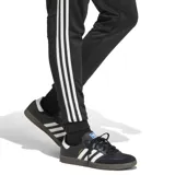 Pantalón deportivo Adidas modelo Tiro Esencial, color negro con las icónicas tres tiras blancas laterales y logo de la marca bordado en la pierna. Cuenta con cintura elástica y puños ajustados en los tobillos.