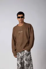 Sweater de punto acanalado color marrón, con cuello redondo, mangas largas y calce relajado. Presenta una estampa pequeña en el centro del pecho.