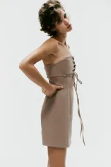 Vestido mini taupe de escote palabra de honor y hombros descubiertos, con detalle de tejido superpuesto y tiras cruzadas ajustables en el pecho. Cuenta con cierre lateral con cremallera oculta.