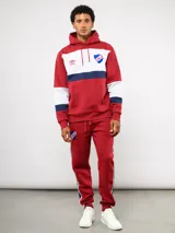 Canguro con capucha de Umbro del Club Nacional de Football, con diseño de bloques de color en azul, blanco y rojo. Presenta bolsillo frontal tipo canguro, cordones ajustables en la capucha y logos bordados del club y la marca.