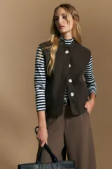 Chaleco de paño color marrón oscuro, de silueta recta y diseño minimalista. Presenta cuello a la base, cierre frontal con botones claros y bolsillos aplicados.