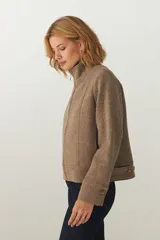 Campera de lana fina sin teñir, con cuello alto, cierre frontal completo y diseño de corte recto con pespuntes decorativos en puños, ruedo y cuello.