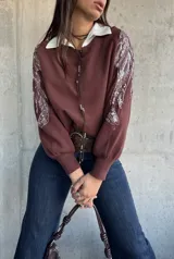 Sweater de punto color chocolate con cuello redondo y mangas largas abullonadas. Presenta detalles bordados con lentejuelas brillantes en los hombros y parte superior de las mangas.