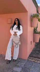 Mochila tipo cartera con tapa, confeccionada en símil cuero color beige. Presenta un diseño moderno con detalle de ojales metálicos en la parte frontal, compartimentos internos organizadores y bolsillo trasero con cierre.