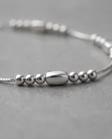 Pulsera de plata 925 fina y delicada con eslabones de cadena y abalorios de cuentas esféricas de diferentes tamaños y un dije central ovalado liso.