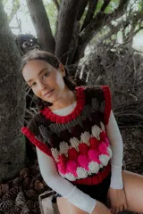 Chaleco tejido de punto con diseño multicolor en bloques, cuello redondo y terminaciones acanaladas. Presenta un patrón geométrico en tonos bordó, rosa, celeste, marrón y crema.