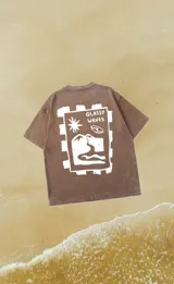 Remera marrón con efecto lavado y estampado en la espalda con la frase "Glassy Waves" y un dibujo de olas, montañas y sol.