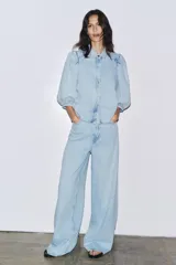 Camisa de denim celeste con cuello solapa, manga corta abullonada y cierre frontal con botones.