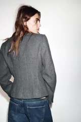 Blazer de corte entallado con cuello redondo, manga larga y hombreras. Presenta cierre frontal con botones dorados y una textura sutil en la tela.