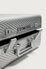 Maleta de cabina rígida fabricada en aluminio con diseño de líneas diagonales en relieve. Cuenta con cuatro ruedas giratorias, cierre TSA, compartimento principal con separador y asa telescópica.