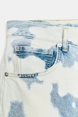 Jeans de tiro medio con corte barrel, confeccionados en algodón con estampado tipo tie-dye en tonos azul y blanco. Presentan diseño de cinco bolsillos, trabillas en la cintura y cierre frontal con cremallera y botón.