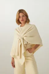 Ruana de tejido de punto industrial, confeccionada en lana fina sin teñir, con diseño de doble ojal para permitir el cruce y cierre frontal.