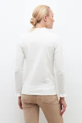 Remera blanca de media polera con mangas largas y volados en los puños.