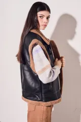 Chaleco negro de cuero sintético con interior de piel sintética color beige, cierre frontal con cremallera y corte oversize.