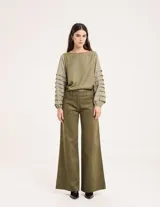 Pantalón de pana color verde oliva, de corte wide leg y largo al tobillo. Tiene cierre delantero con botón, bolsillos laterales y traseros.