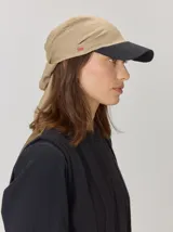 Gorro tipo pañuelo con visera rígida azul marino, confeccionado en lino con estampado de rayas grises y blancas. Presenta un diseño envolvente con caída trasera y detalle de logo bordado en el lateral.