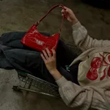 Cartera baguette roja con textura croco, cierre superior con cremallera y correa de hombro corta.