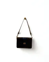 Minibag bandolera de cuero negro con acabado brillante, correa ajustable y cierre metálico frontal tipo torniquete.