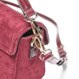 Bandolera color bordó de símil gamuza con solapa frontal y cierre magnético. Presenta un detalle frontal con el logo "XL" en dorado, asa corta desmontable y correa larga regulable y desmontable. Incluye herrajes metálicos dorados y un bolsillo interno con cierre.