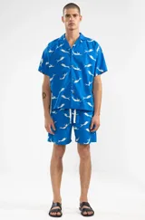 Short de algodón azul con estampado de sirenas blancas, corte relajado y largo hasta la rodilla. Tiene cintura elástica con cordón ajustable, dos bolsillos laterales y un bolsillo trasero tipo parche.