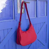 Cartera tipo hobo o media luna de cuero sintético negro, con textura granulada. Posee una correa ajustable para llevar al hombro o cruzada.