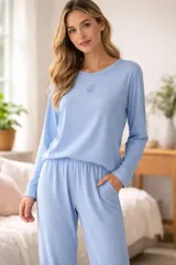 Pijama de dos piezas en color celeste, compuesto por una remera de manga larga con cuello redondo y un pequeño bordado en el pecho, y un pantalón con cintura elástica y bolsillos laterales. Confeccionado en tejido de punto acanalado.