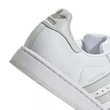 Championes adidas Superstar de diseño icónico con exterior de cuero sintético blanco, las tres tiras laterales en tono gris claro y la clásica puntera de goma con relieve.