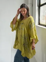 Blusa color verde pistacho, de corte holgado, manga corta con volados y diseño asimétrico con volado en el ruedo. Cuenta con un estampado floral difuminado en el frente.