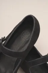 Zapato plano estilo Mary Jane de cuero negro, con punta fina y tira ajustable con hebilla sobre el empeine.