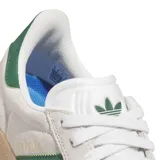 Championes Adidas modelo Gazelle ADV, con diseño clásico de perfil bajo. Presentan una capellada de gamuza en color beige claro, con las icónicas tres tiras laterales y refuerzo en el talón en color verde oscuro. Incluyen cordones blancos, suela de goma color caramelo y el nombre del modelo estampado en dorado en el lateral.