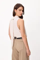 Blusa sin mangas color crema, con cuello alto fruncido y diseño holgado.