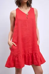 Vestido corto blanco sin mangas, con escote en V y detalle de broche dorado en el centro. La falda tiene un volado en el ruedo.