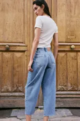 Jeans de tiro alto con corte barrel, pernera holgada que se estrecha hacia el tobillo y bajo deshilachado. Presenta costuras verticales decorativas en el frente y cierre frontal con cremallera y botón.