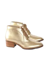 Botín de caña baja con cordones, confeccionado en cuero vacuno metalizado color dorado. Presenta puntera redondeada y tacón bloque texturizado en tono madera.
