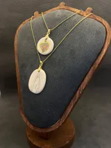 Collar de cadena fina dorada con dije ovalado de cerámica en tono crema, ilustrado con la figura de la Virgen.