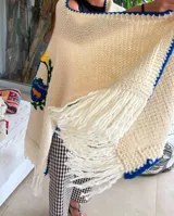 Ruana de lana merino color crema, tejida y bordada a mano, con el escudo de Uruguay en la espalda y flecos en el ruedo.