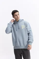 Canguro con capucha de algodón color celeste, con estampa gráfica en la espalda que incluye flores y la frase 'Grow Back'. Presenta un parche pequeño en la manga y corte regular.