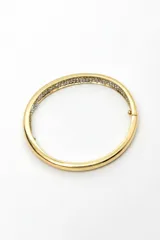 Pulsera rígida tipo brazalete dorado con detalles de circones engastados en el borde interior.
