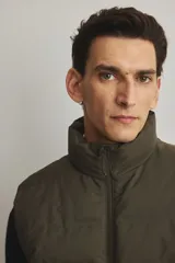 Chaleco acolchado color verde militar, con cuello alto, cierre frontal y bolsillos laterales con cierre.