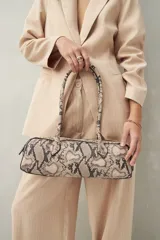 Cartera baguette cilíndrica con estampado de piel de serpiente en tonos beige y negro. Asas cortas y cierre superior con cremallera.
