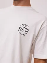 Remera blanca de algodón con cuello redondo y manga corta. Presenta un pequeño estampado frontal con el logo de Rusty y un diseño de tabla de surf.