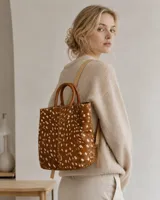 Mochila de cuero con pelo y estampado animal print símil ciervo, con asas superiores de mano y correas traseras ajustables.