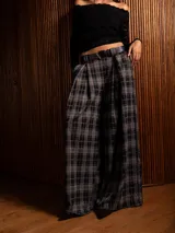 Pantalón tipo palazzo de corte amplio y tiro alto, con diseño de estampado a cuadros tipo tartán en tonos oscuros. Presenta pinzas en la cintura y bolsillos laterales.