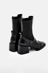 Bota tipo chelsea de cuero color bordó, con paneles elásticos laterales negros, puntera cuadrada y taco bloque negro.