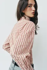 Camisa de rayas rojas y blancas, cuello redondo con lazada integrada y manga larga.