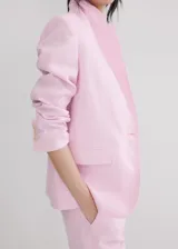 Blazer de lino color rosado, de diseño recto con cuello en pico y solapas con muesca. Cuenta con manga larga, dos bolsillos de ribete delanteros y cierre frontal de un botón.