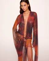 Minivestido cruzado con estampado animal print en tonos naranja, marrón y negro. Tiene escote en V pronunciado, mangas largas acampanadas y falda ajustada.