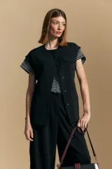 Chaleco negro de corte estructurado con cuello redondo, cierre frontal oculto y lazo ajustable en la cintura. Presenta dos bolsillos frontales con solapa y diseño de hombros caídos.