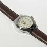 Reloj analógico con caja plateada, esfera blanca con números arábigos y correa marrón de cuero.